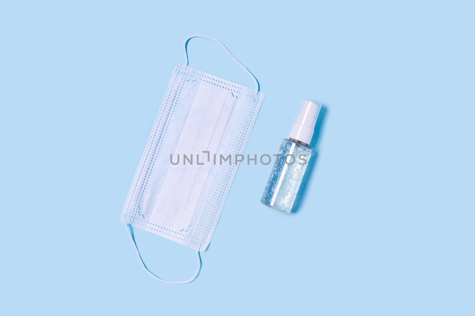 Flat lay with a medical mask placed in the center, a bottle of antiseptic soap or hand sanitizer.