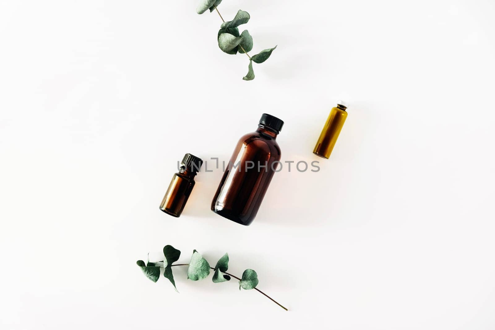 Two bottles of fragrant cosmetic or essential oil on a white background surrounded by sprigs of eucalyptus. Stay home and be mentally healthy.