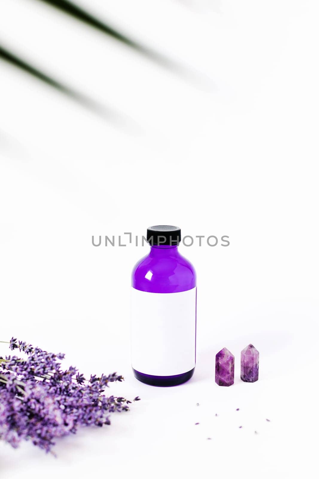 Glass bottle with body lotion, aroma oil on white background surrounded by lavender and the crystal of quartz.