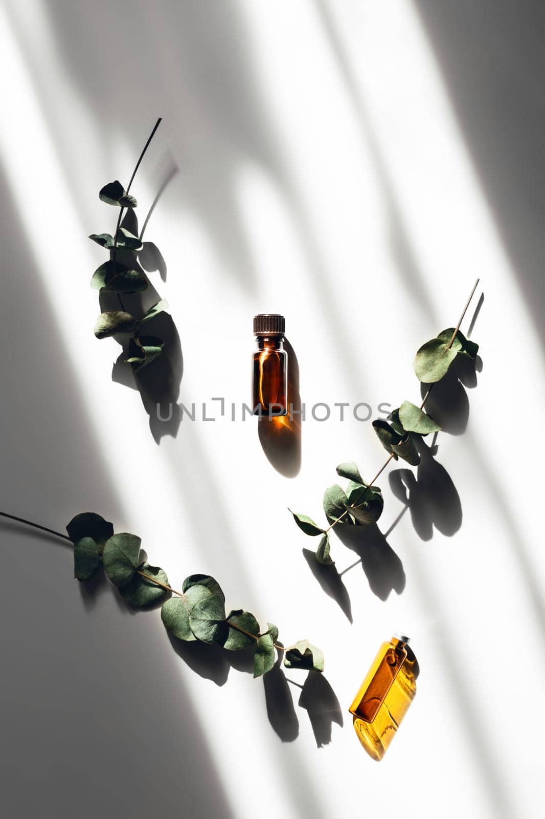 Stay at home and be mentally balanced with aromatherapy. Two bottles of aromas lying on a white table in the shade from the sun and surrounded by eucalyptus.