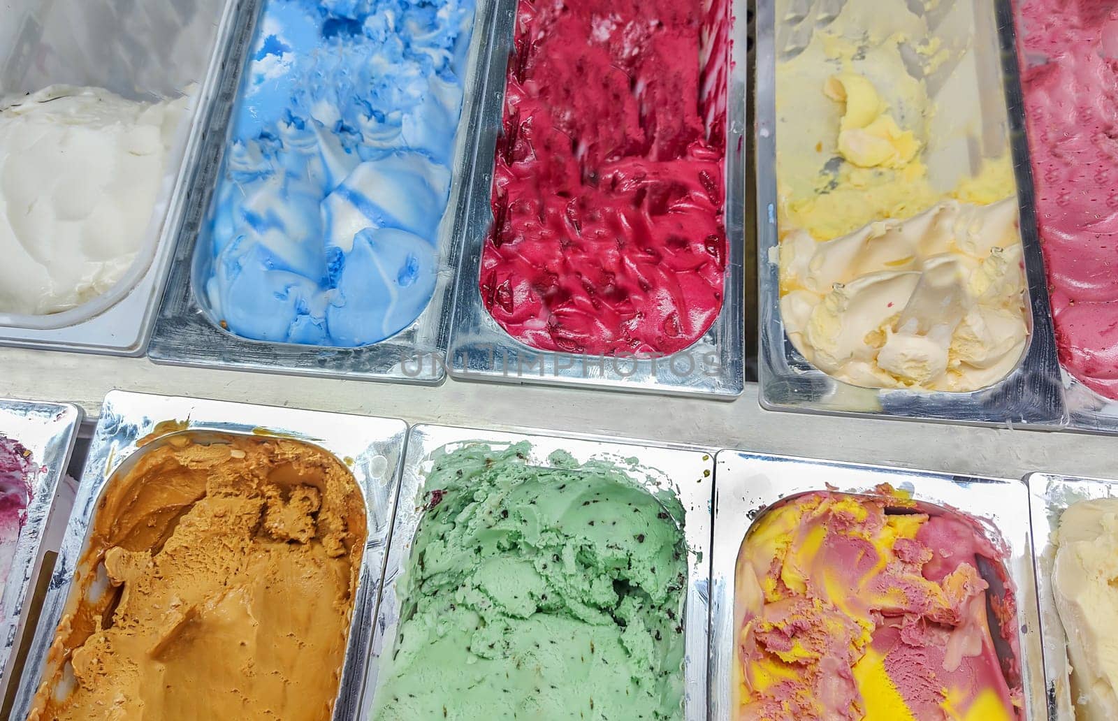 Big range of ice cream of various varieties and colors in metal containers on shop window.