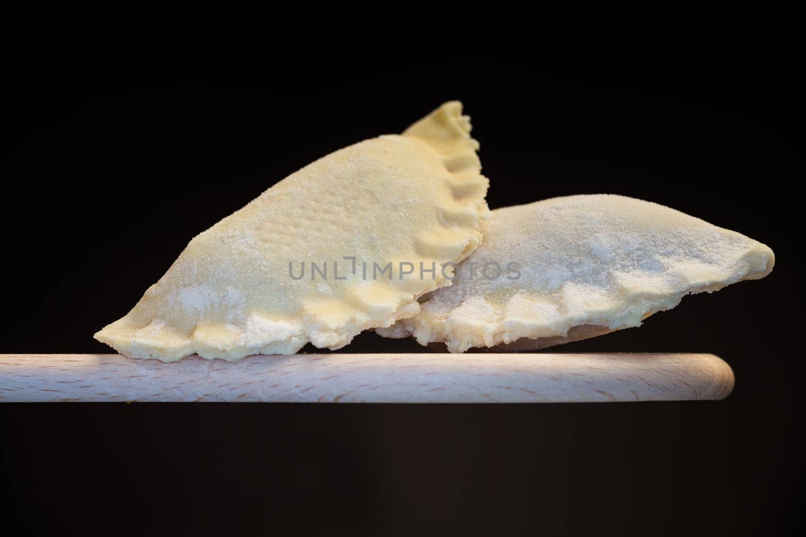 Raw dumplings with filling inside, Ukrainian cuisine. Raw dumplings for freezing on a wooden spoon isolated on a black background. Home kitchen.