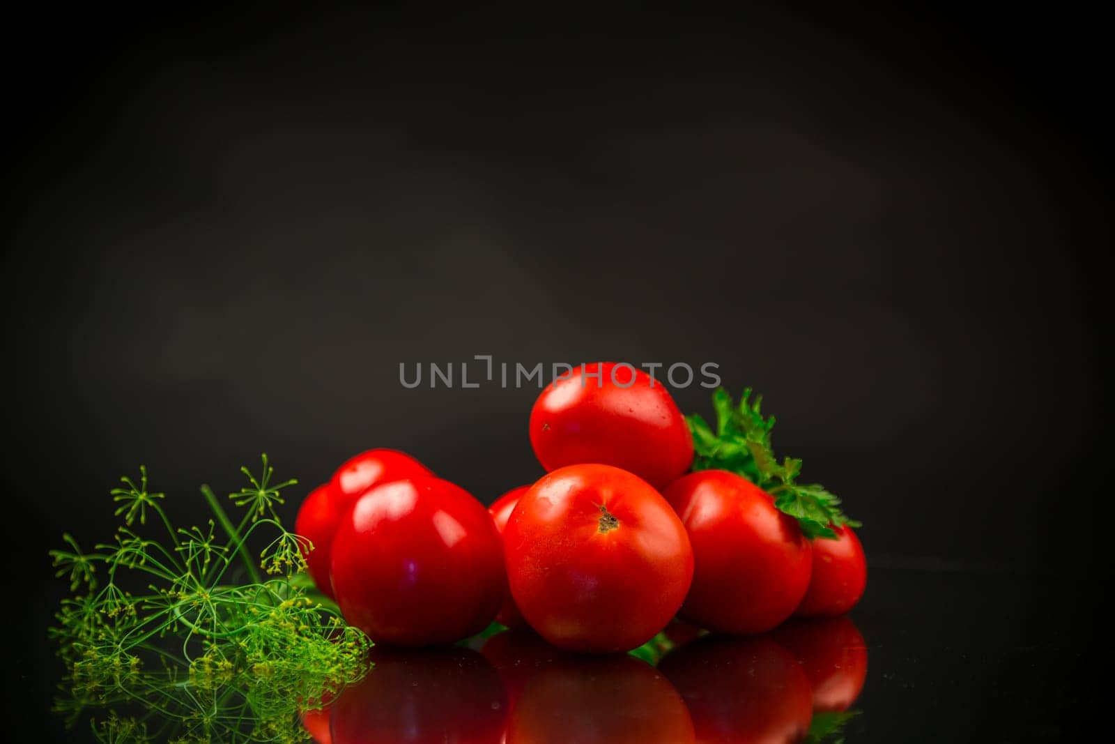 Ripe red tomatoes with greens, isolated on black background.