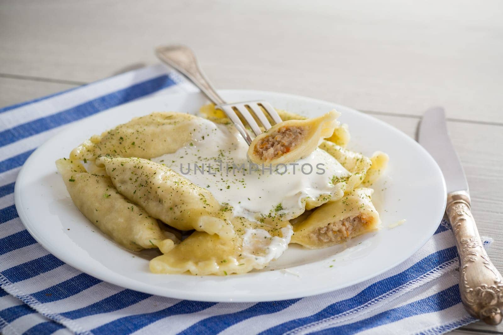 cooked dumplings with meat, spices and sour cream, in a plate on a light wooden table. Ukrainian food.