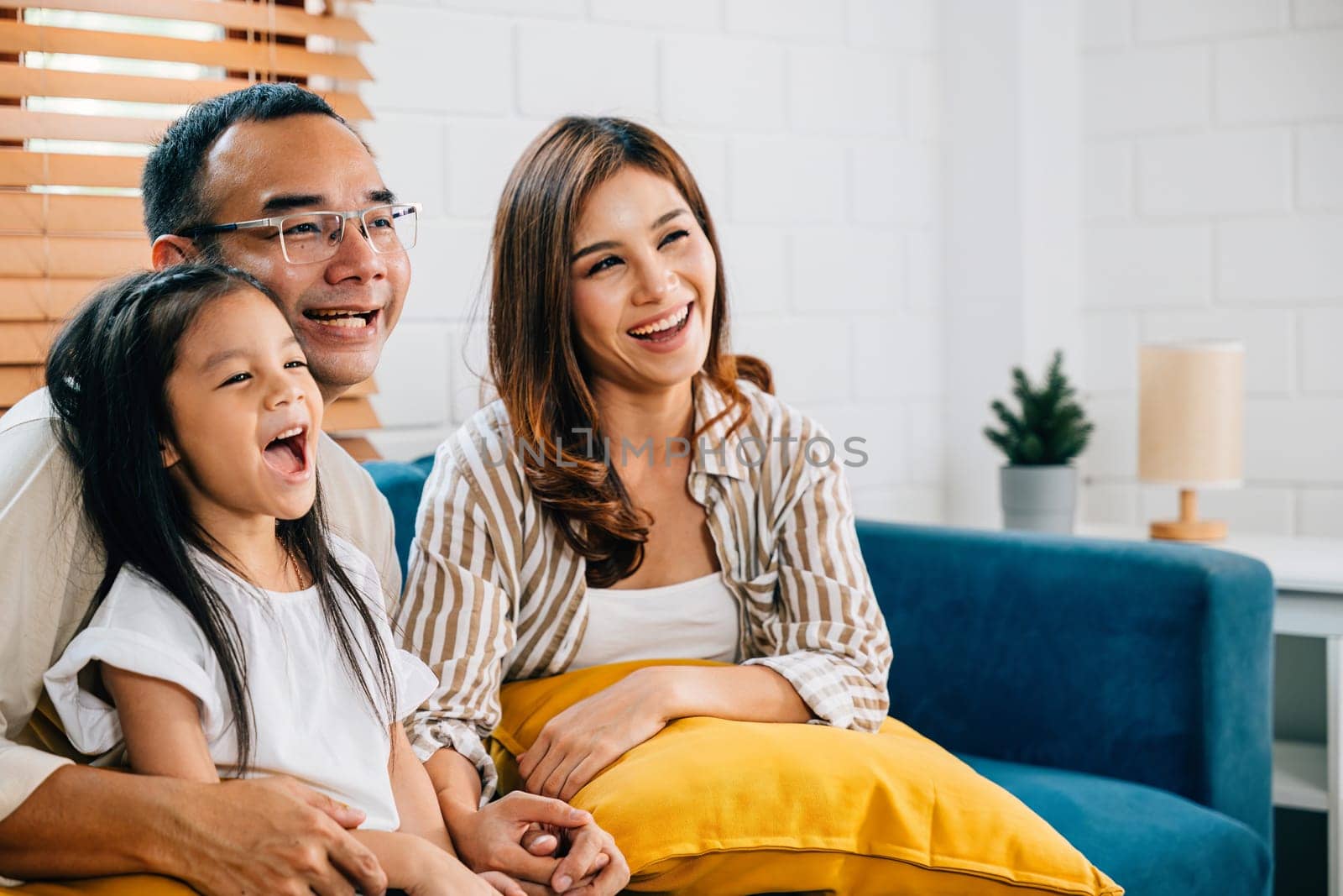 In their modern grooved house happy Asian family enjoys quality family time watching TV together on sofa. father mother son and daughter share laughter joy and togetherness during their weekend.