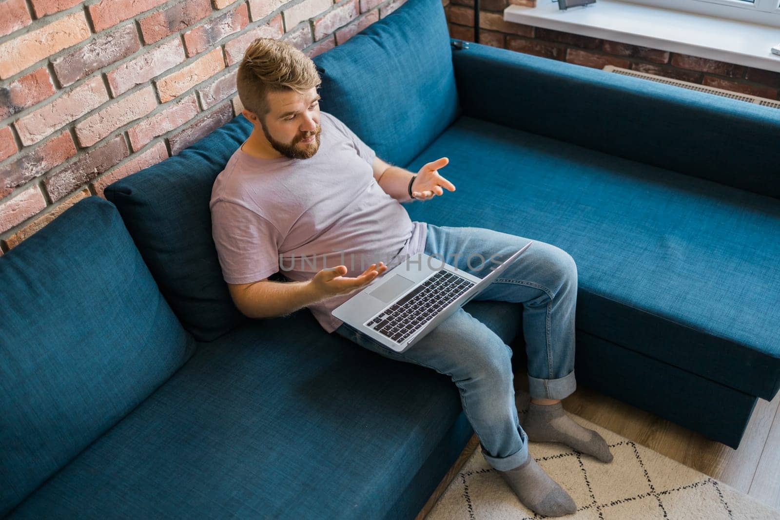 Young man at home on the couch talking by video call with a laptop. Technologies and communication online