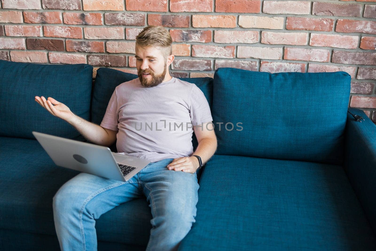 Young man at home on the couch talking by video call with a laptop. Technologies and communication online