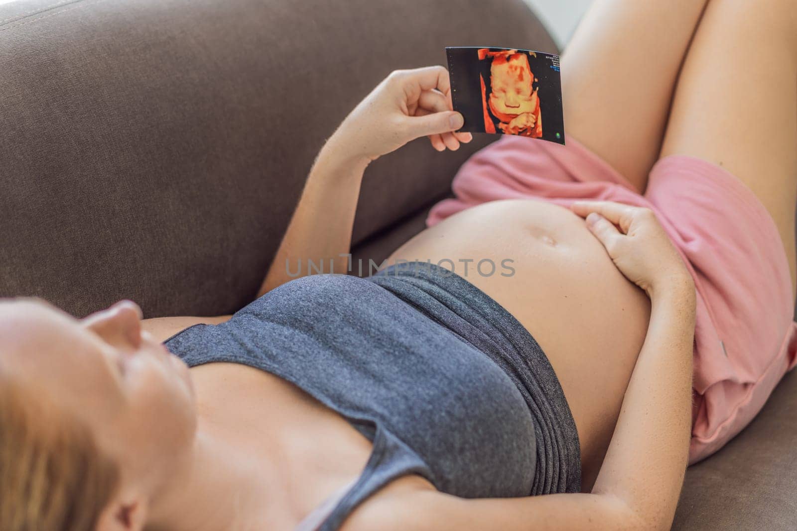 Expectant mother tenderly connects with her unborn child, holding ultrasound photo to her pregnant belly by galitskaya