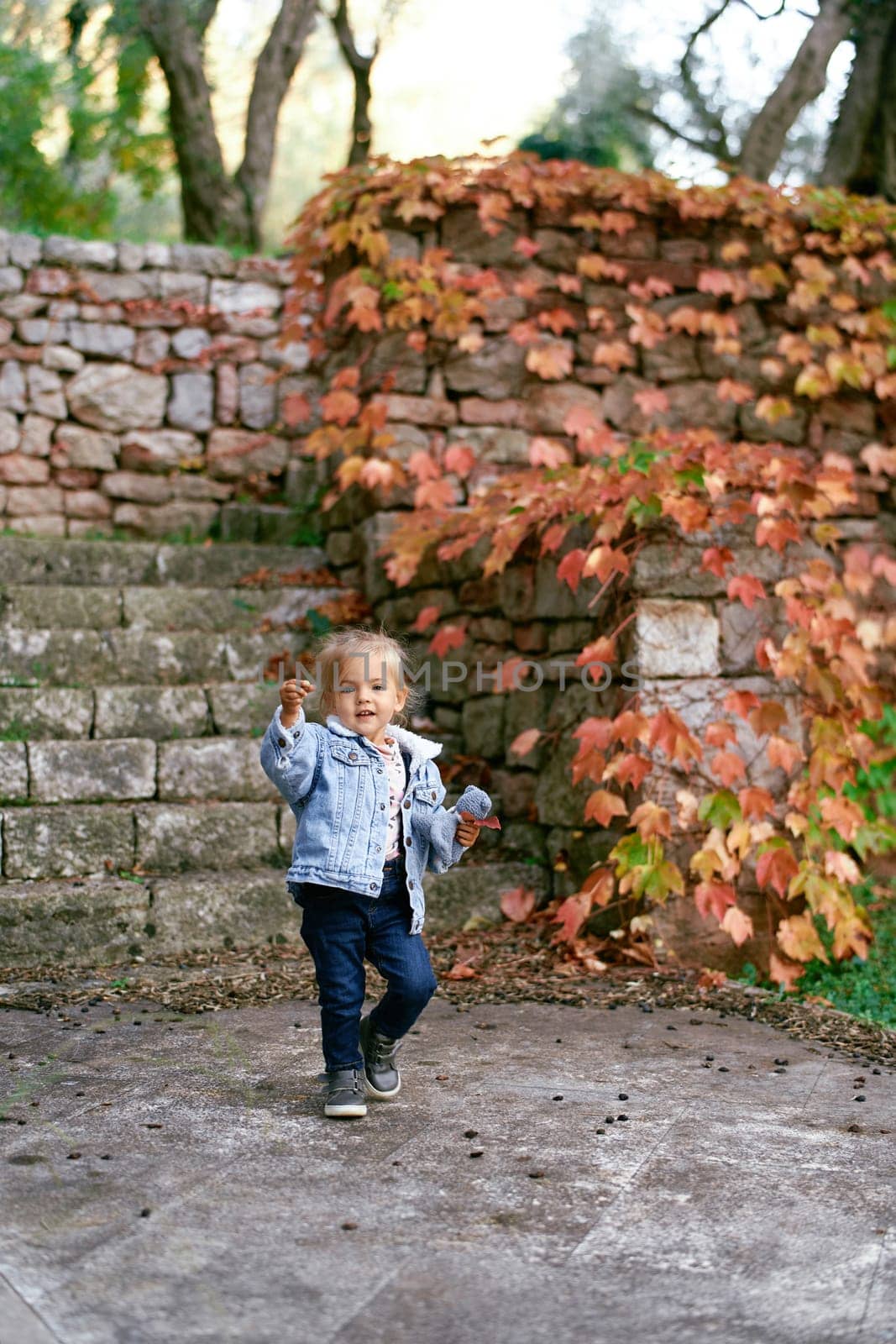 Little girl with a soft toy in her hand walks along a paved path near the steps in the park. High quality photo