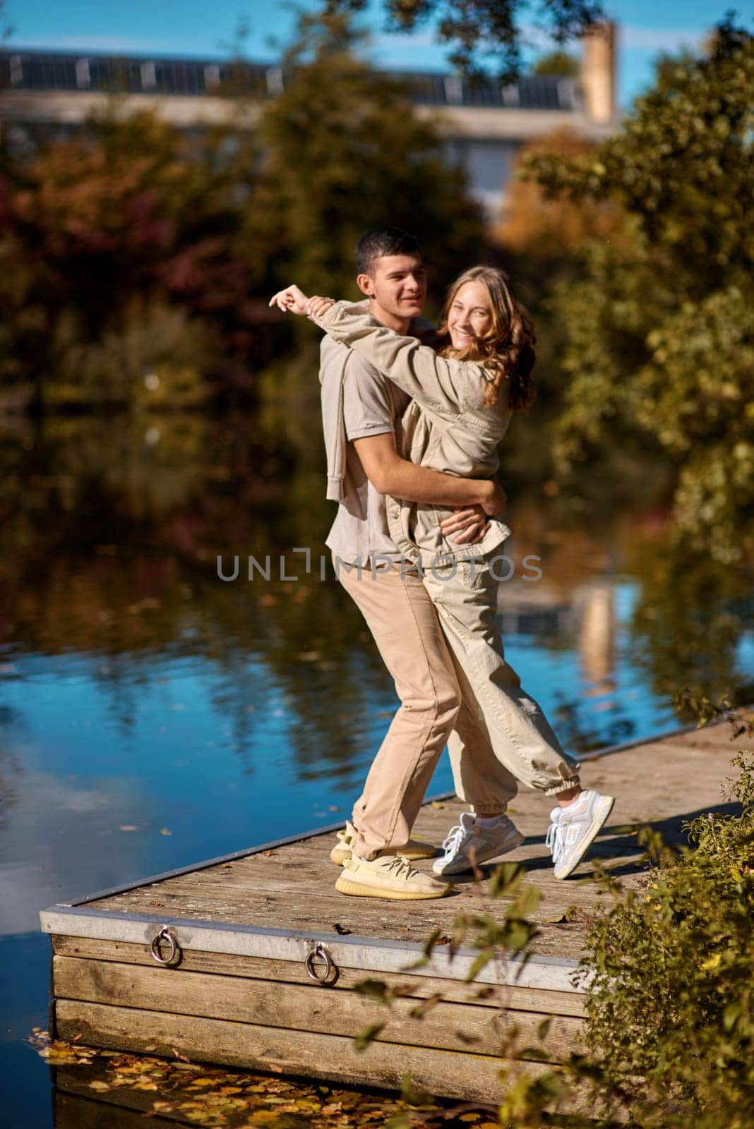 A happy couple in love in casual clothes travel together, hike and have fun in the fall forest on a weekend in nature in autumn outdoors, selective focus. Handsome man embracing with passion his girlfriend outdoor under the leaves of trees on the embankment. Love history. Happy people concept