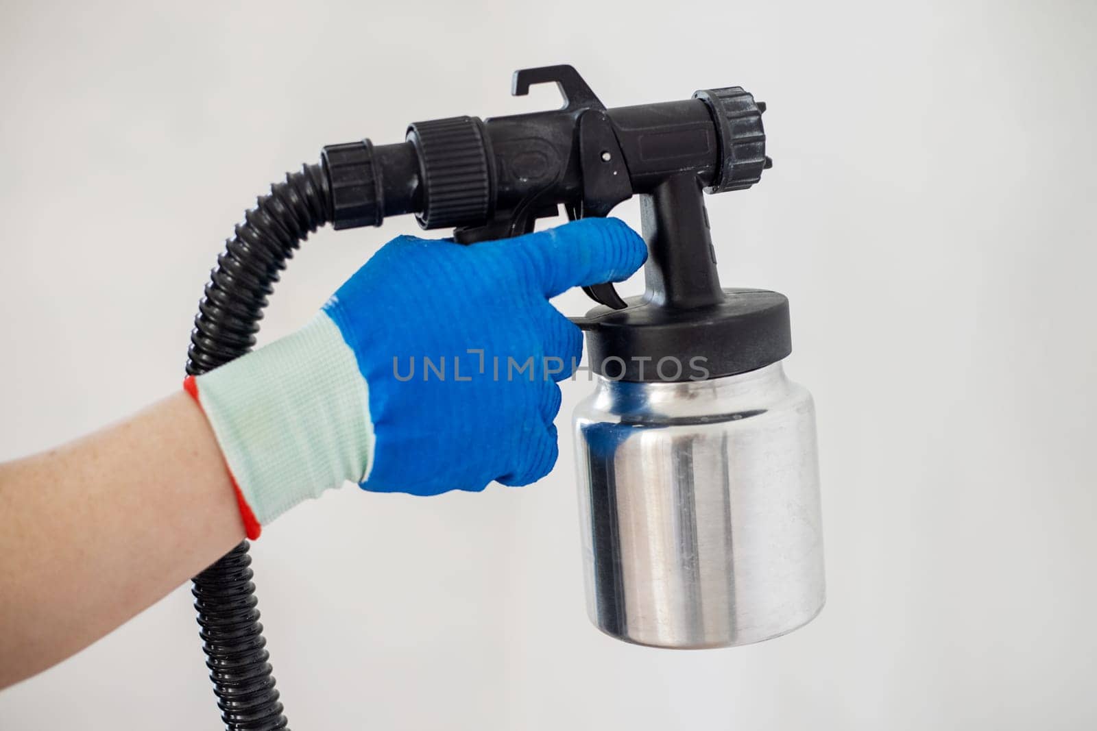 Man's hand in protective glove paint a wall with an electric spray gun. Electric spray painting. Repair of the apartment