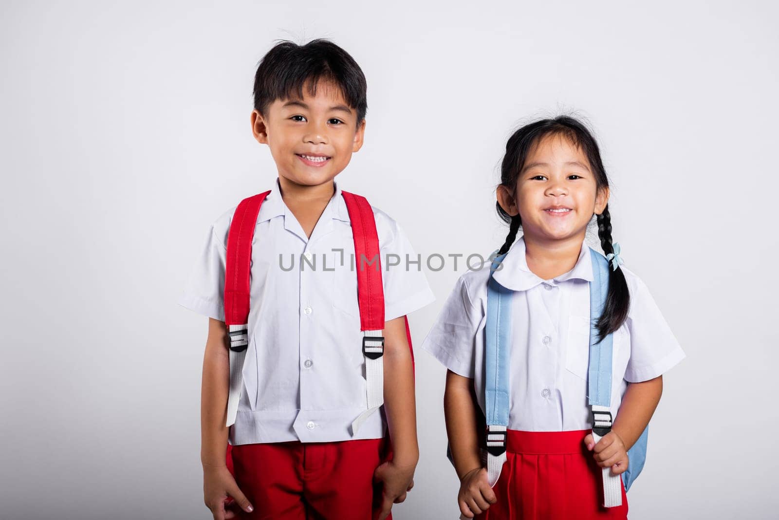 Two Asian student kid girl boy schoolchildren brother sister smile happy wear student thai uniform red pants skirt by Sorapop