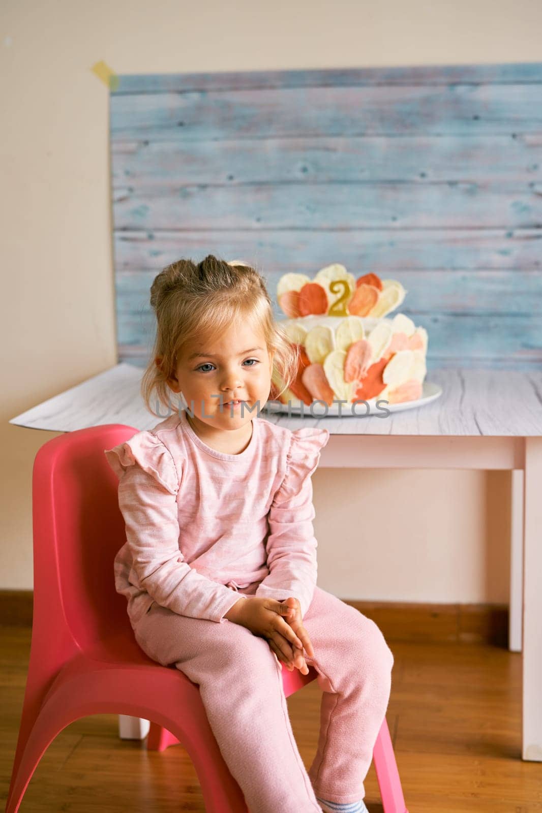 Little smiling girl sitting on chair near table with birthday cake by Nadtochiy