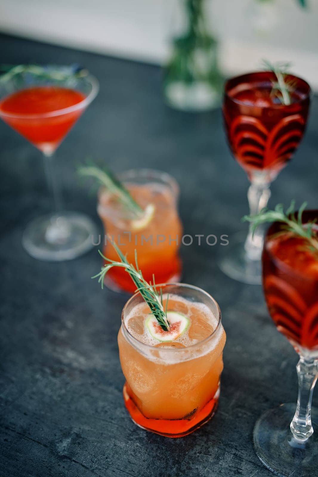 Orange cocktails in glasses with green twigs and pieces of fruit stand on the table by Nadtochiy