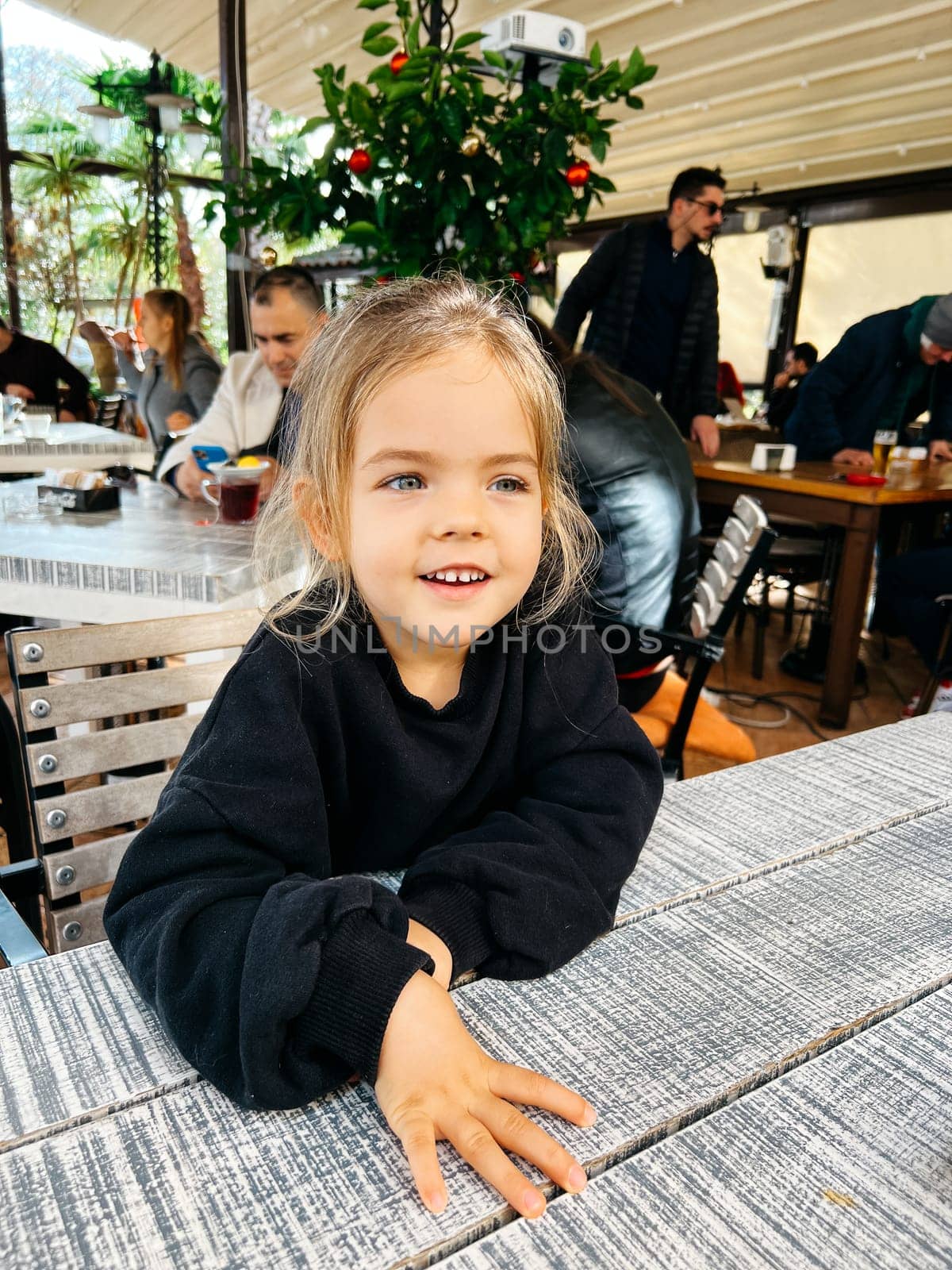 Little smiling girl sitting at a table in a restaurant. High quality photo