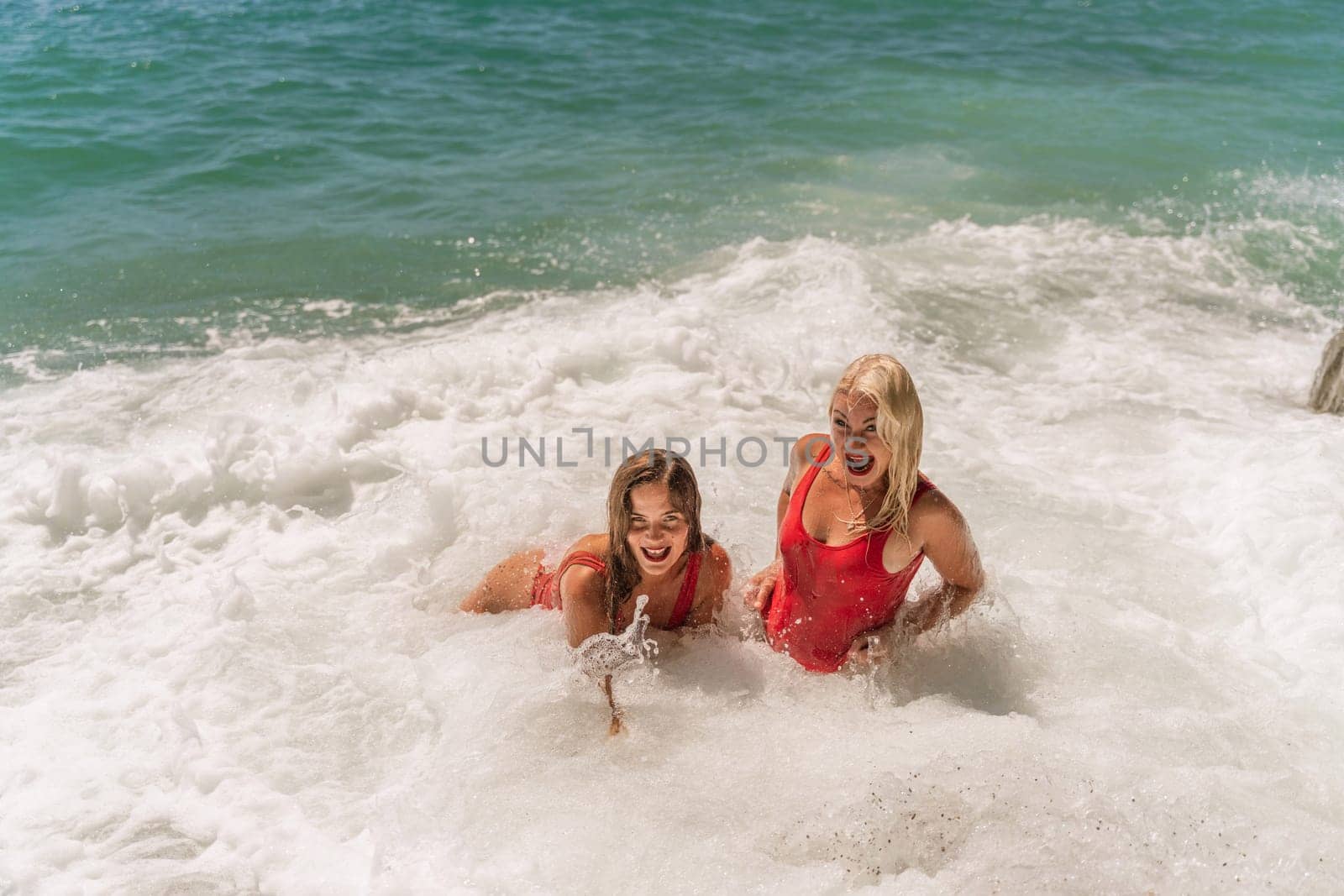 Women ocean play. Seaside, beach daytime, enjoying beach fun. Two women in red swimsuits enjoying themselves in the ocean waves. by Matiunina