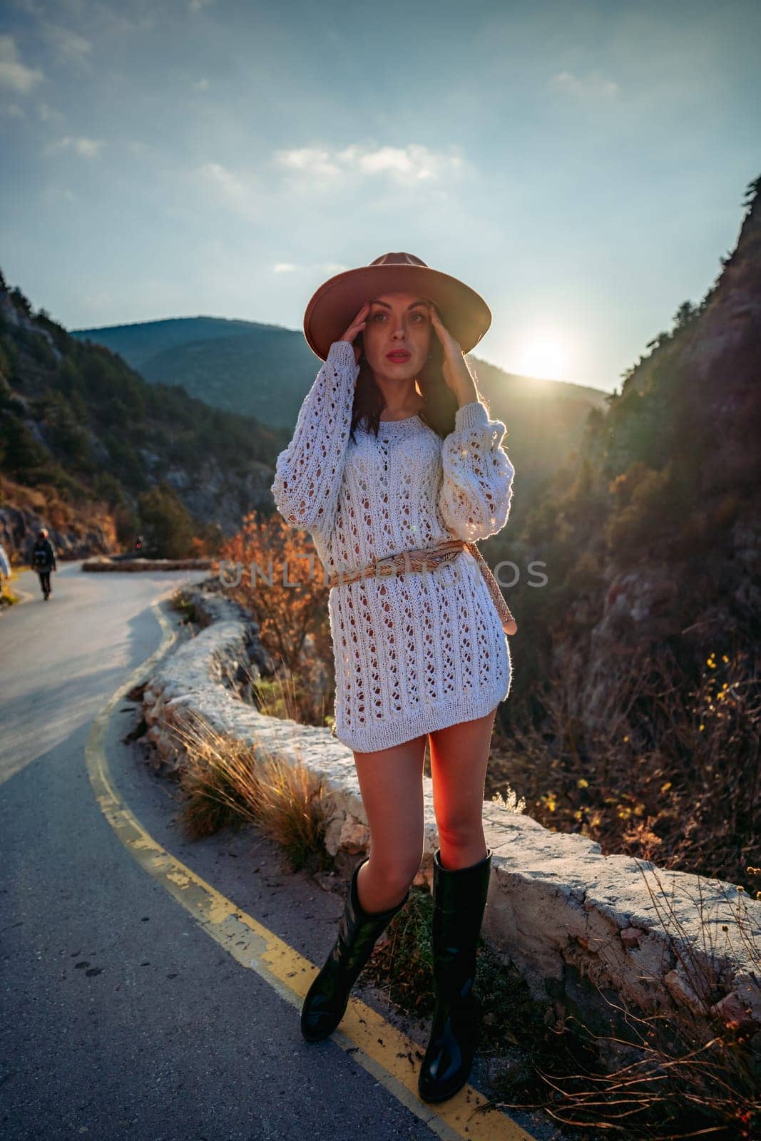Woman road mountain. A woman in a white sweater, black boots and a hat walks along a winding alpine path between the mountains at sunset in late summer. The concept of travel. by Matiunina