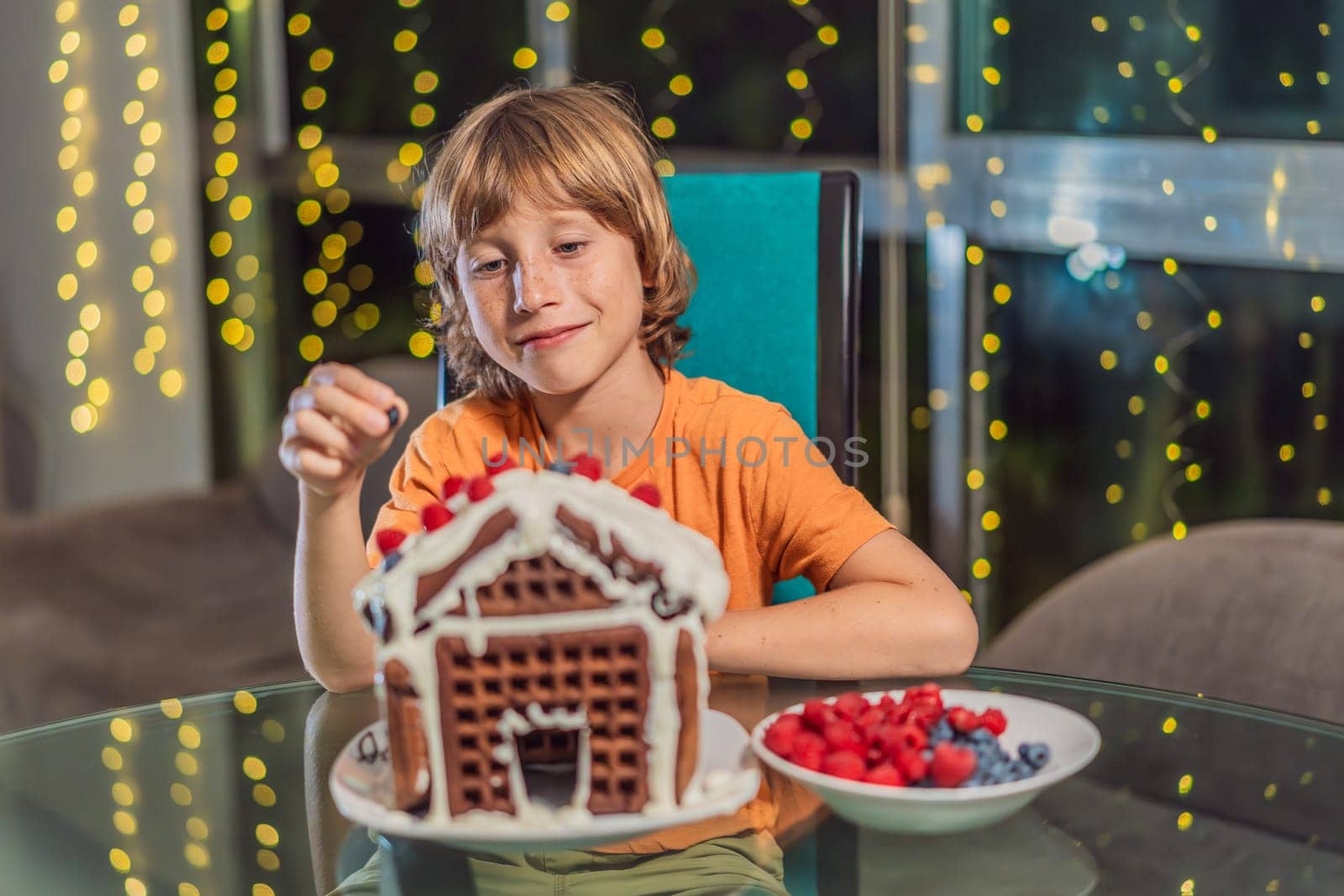 Immerse in festive delight as a boy crafts boy crafting an unconventional gingerbread house, infusing Christmas with unique creativity and festive cheer. A sweet scene of seasonal bonding and culinary fun by galitskaya