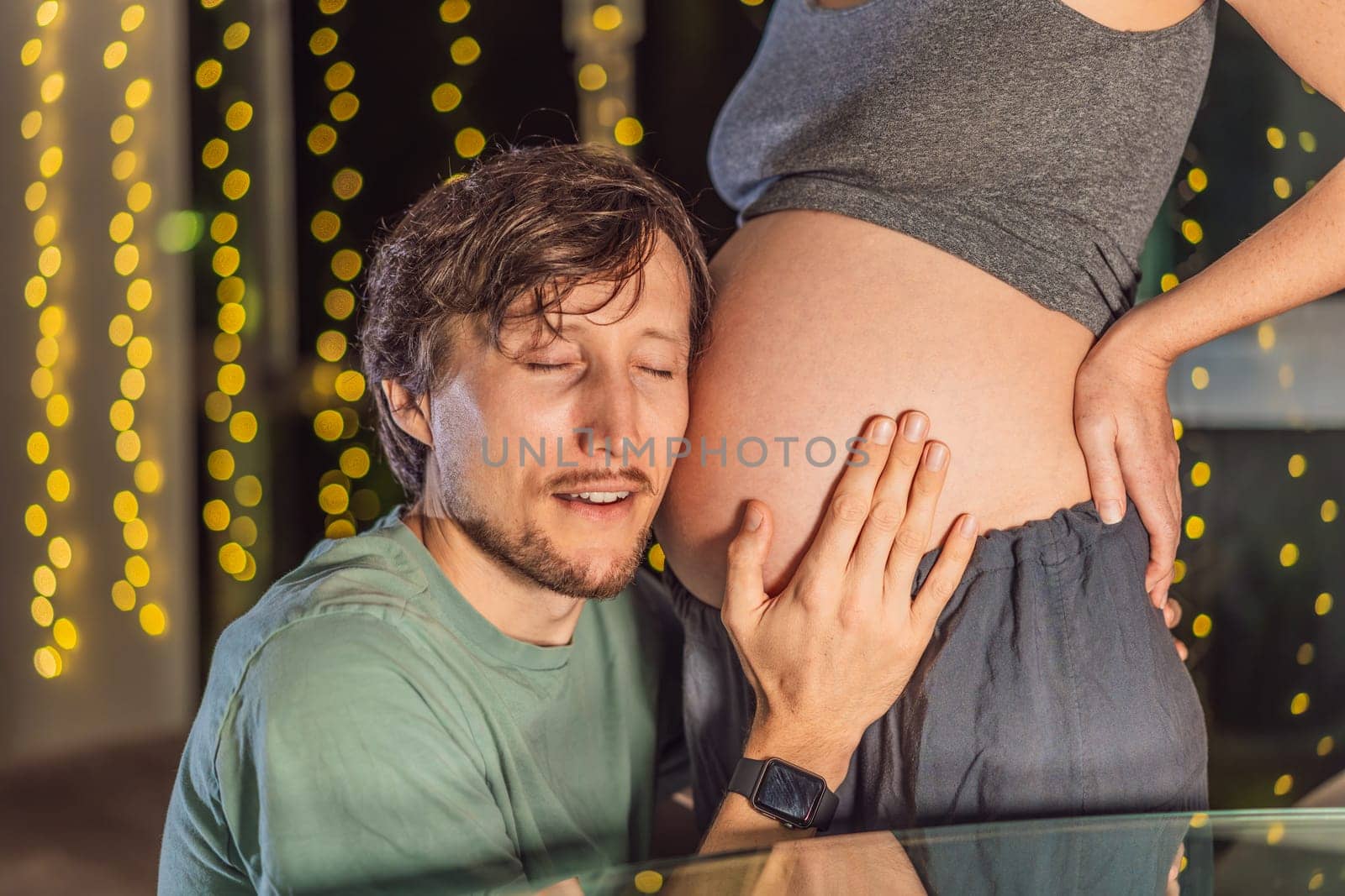 In a tender holiday moment, a husband kisses his wife's pregnant belly, expressing love and anticipation for the Christmas joy to come.