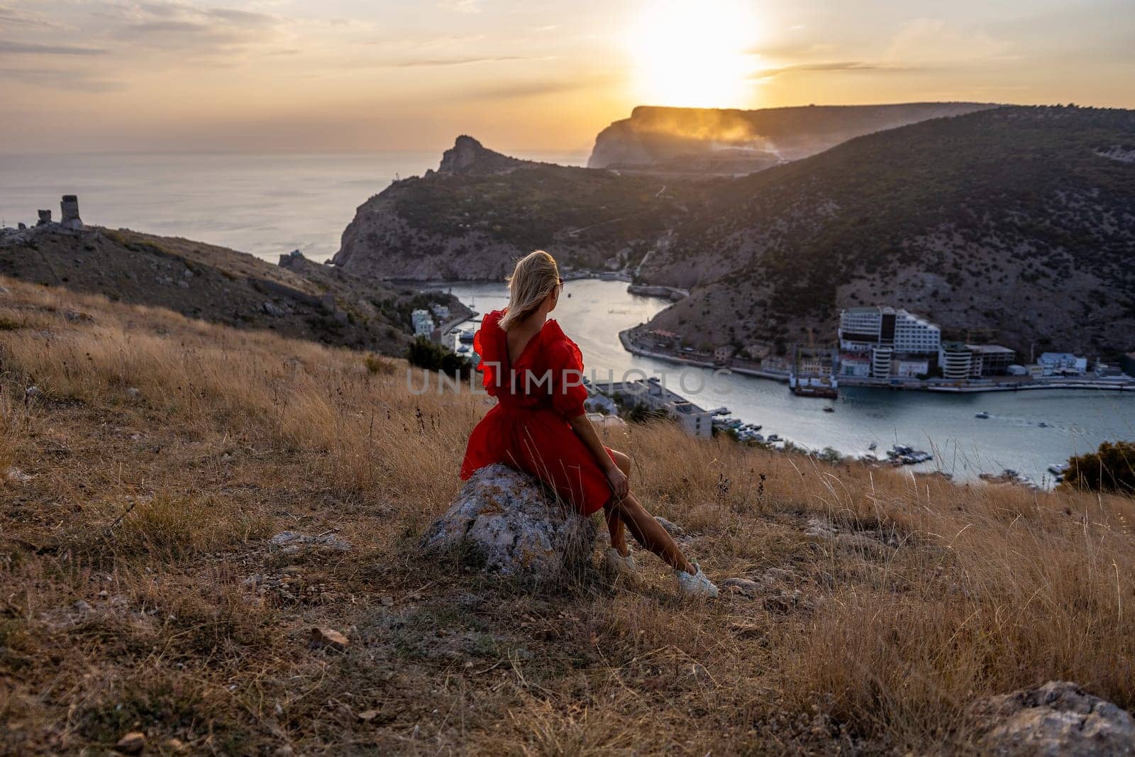 Woman sunset sea mountains. Happy woman siting with her back on the sunset in nature summer posing with mountains on sunset, silhouette. Woman in the mountains red dress, eco friendly, summer landscape active rest.