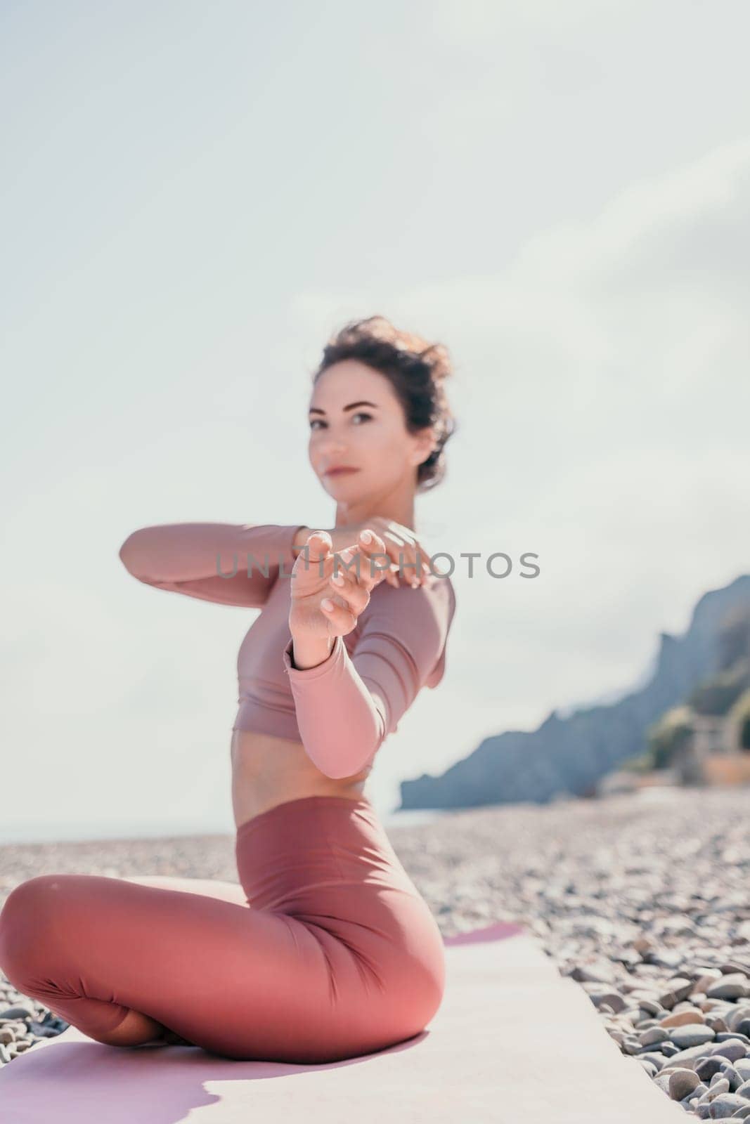 Young woman with long hair in white swimsuit and boho style braclets practicing outdoors on yoga mat by the sea on a sunset. Women's yoga fitness routine. Healthy lifestyle, harmony and meditation