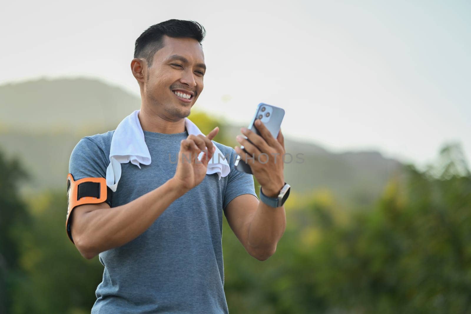 Smiling sporty man checking training results on mobile app after running in the park. Technology health and wellness concept.
