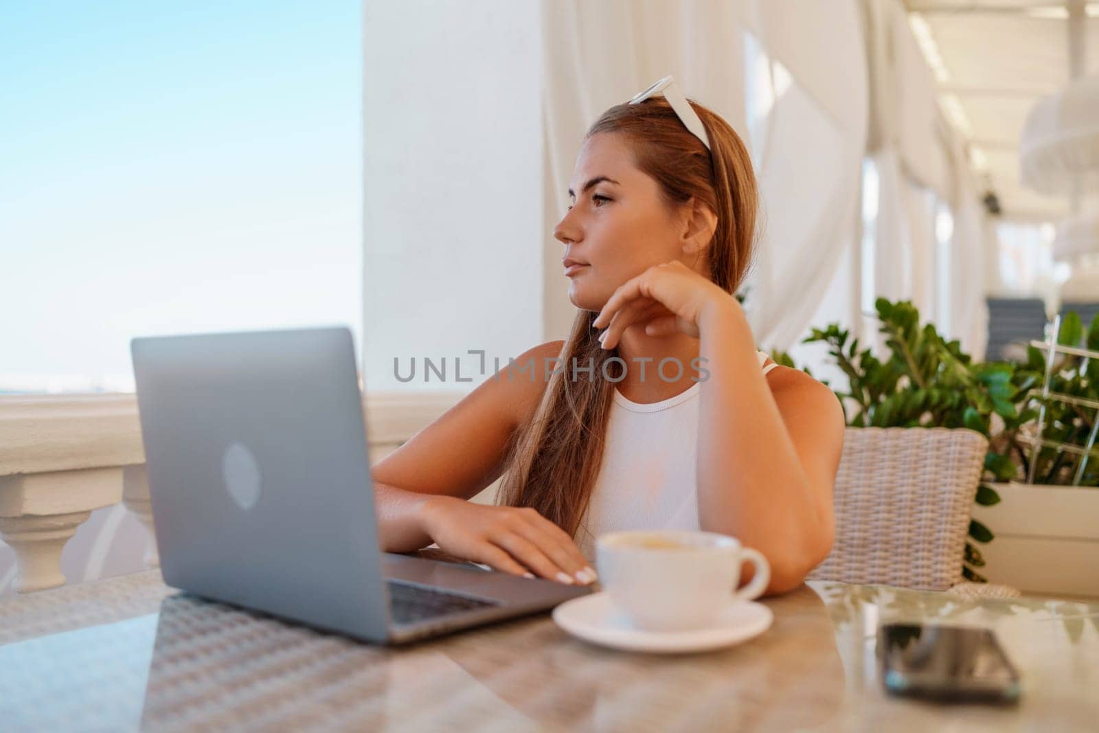 Woman coffee cafe laptop. Coffee break in cafe. Tranquil long haired woman drinking coffee in plant filled place. Woman sitting at a coffee shop with mobile phone drinking coffee