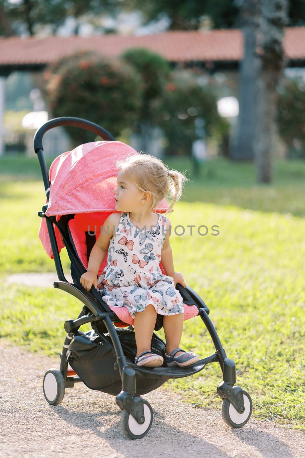 Little girl sitting in a stroller in the park looking back. High quality photo