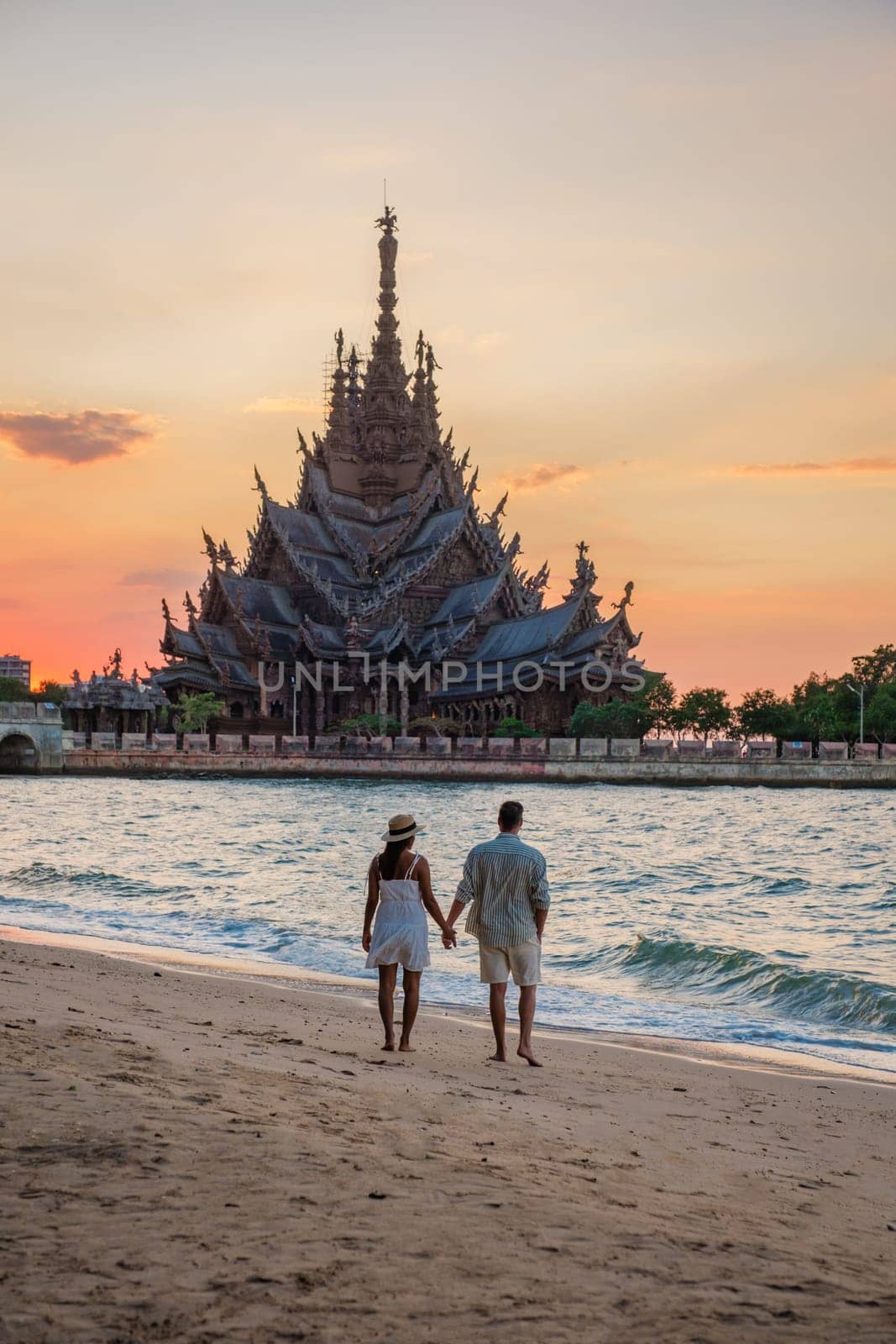 A diverse multiethnic couple of men and women visit The Sanctuary of Truth wooden temple in Pattaya Thailand. a wooden temple construction located at the cape of Naklua Pattaya City Chonburi Thailand