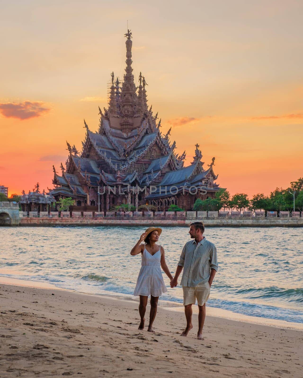 A diverse multiethnic couple of European men and Asian women visit The Sanctuary of Truth wooden temple in Pattaya Thailand at sunset