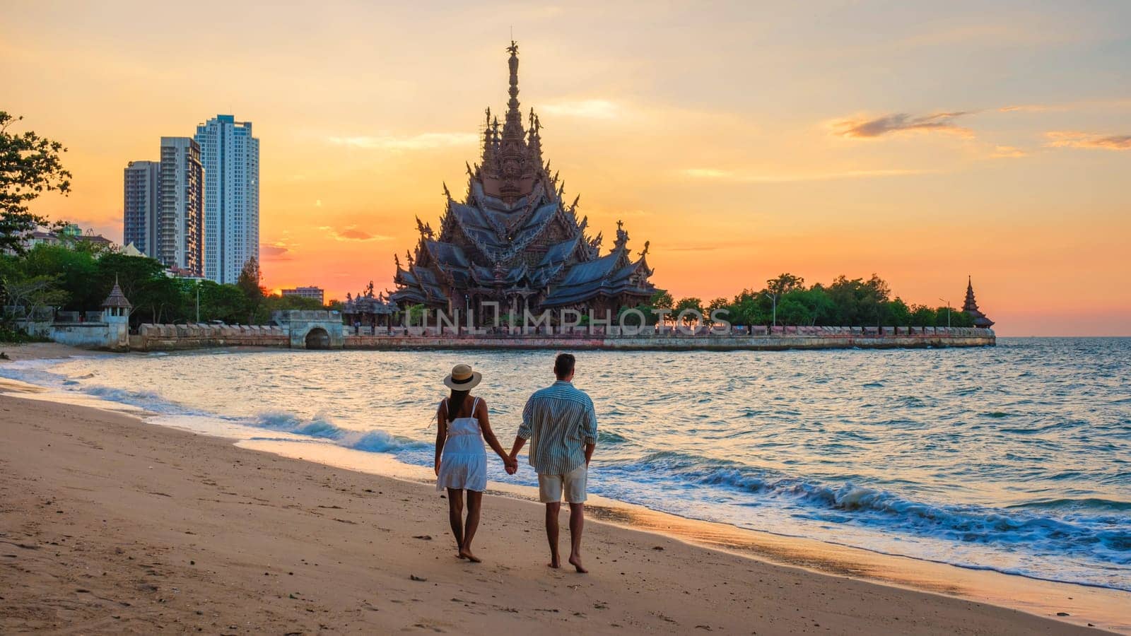 A diverse multiethnic couple of European men and Asian women visit The Sanctuary of Truth wooden temple in Pattaya Thailand at sunset