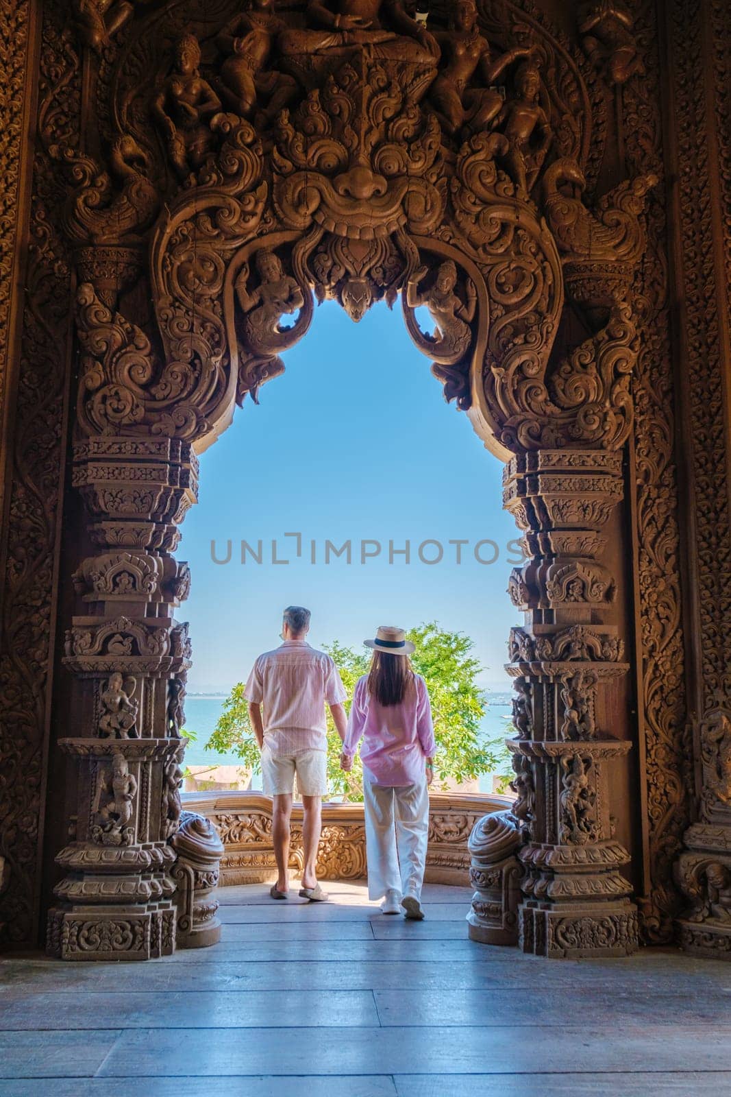 A diverse multiethnic couple of Caucasian men and Asian women visit The Sanctuary of Truth wooden temple in Pattaya Thailand. It is a wooden temple construction located at the cape of Naklua Pattaya