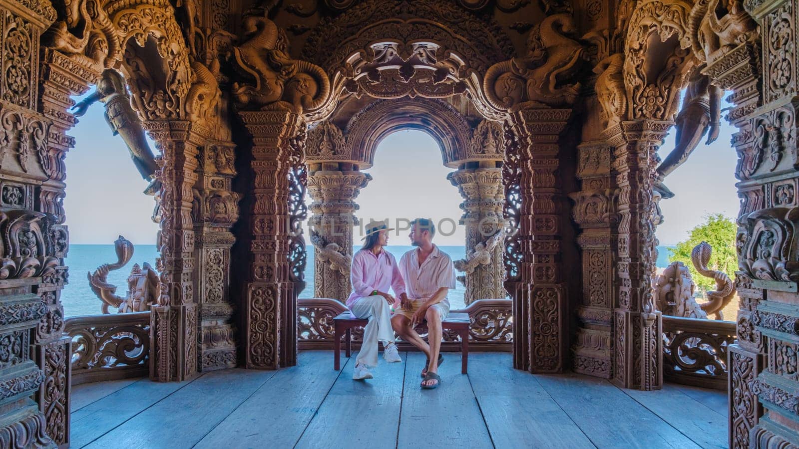 A diverse multiethnic couple of Caucasian men and Asian women visit The Sanctuary of Truth wooden temple in Pattaya Thailand. It is a wooden temple construction located at the cape of Naklua Pattaya