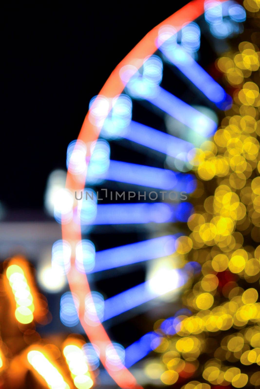 Ferris wheel decorated blue illumination and large Christmas tree decorated yellow illumination on black background at night. Beautiful New Year and Christmas holiday blurred background