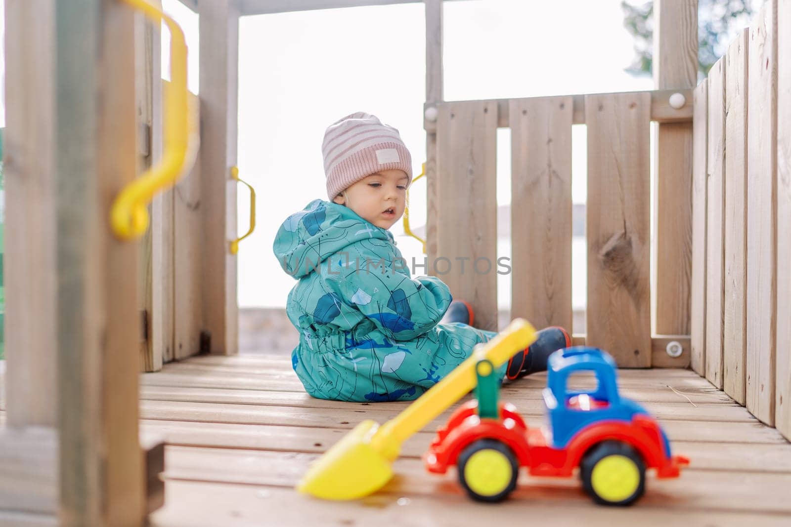 Little girl sits on a wooden slide and looks at a toy car by Nadtochiy
