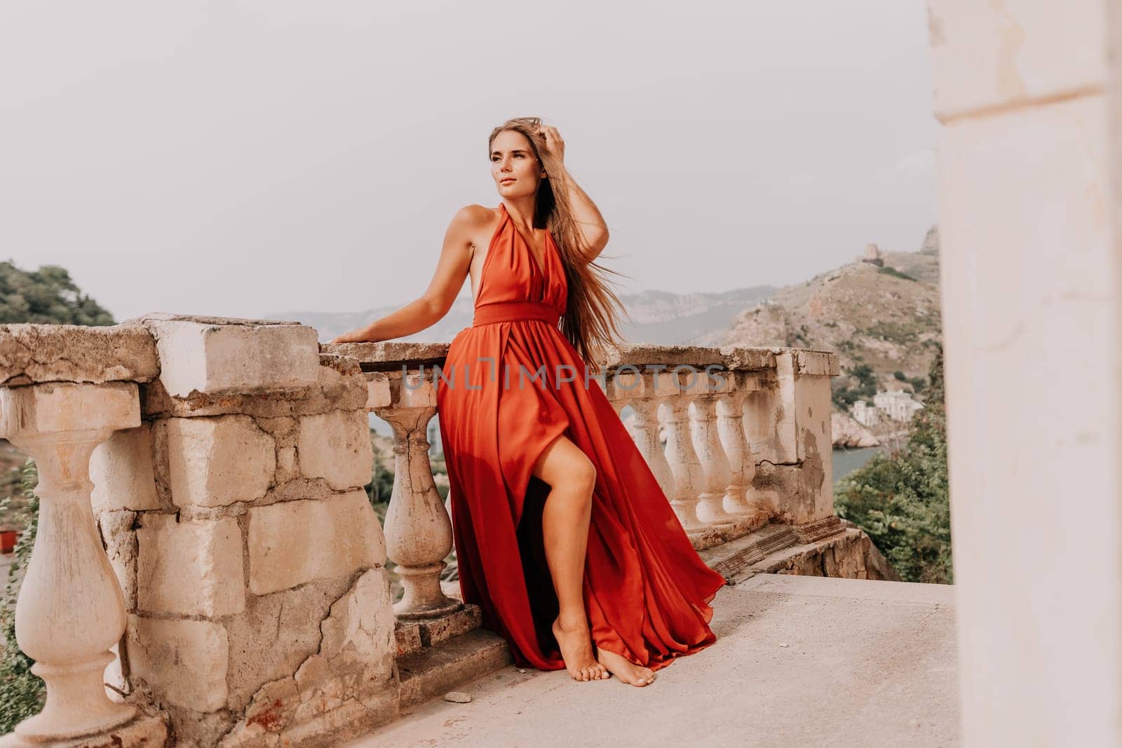 Woman travel portrait. Happy woman with long hair looking at camera and smiling. Close up portrait cute woman in a res long dress posing on backdrop of old travel city near sea by panophotograph