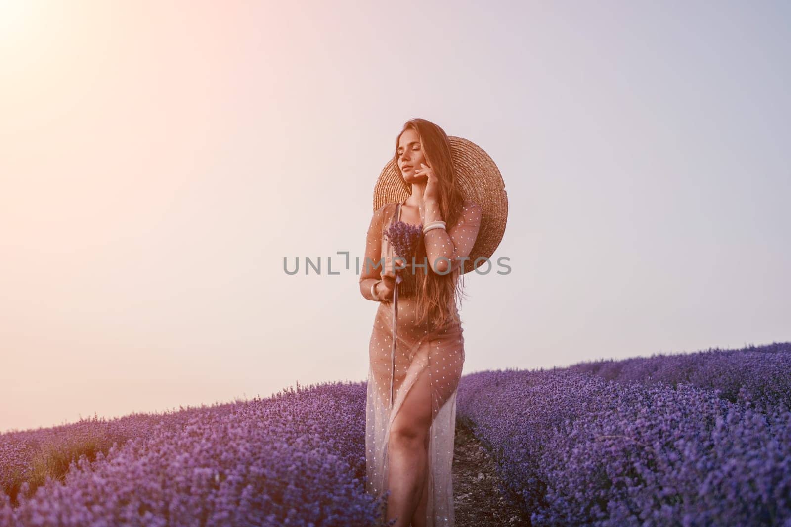 Close up portrait of young beautiful woman in a white dress and a hat is walking in the lavender field and smelling lavender bouquet.