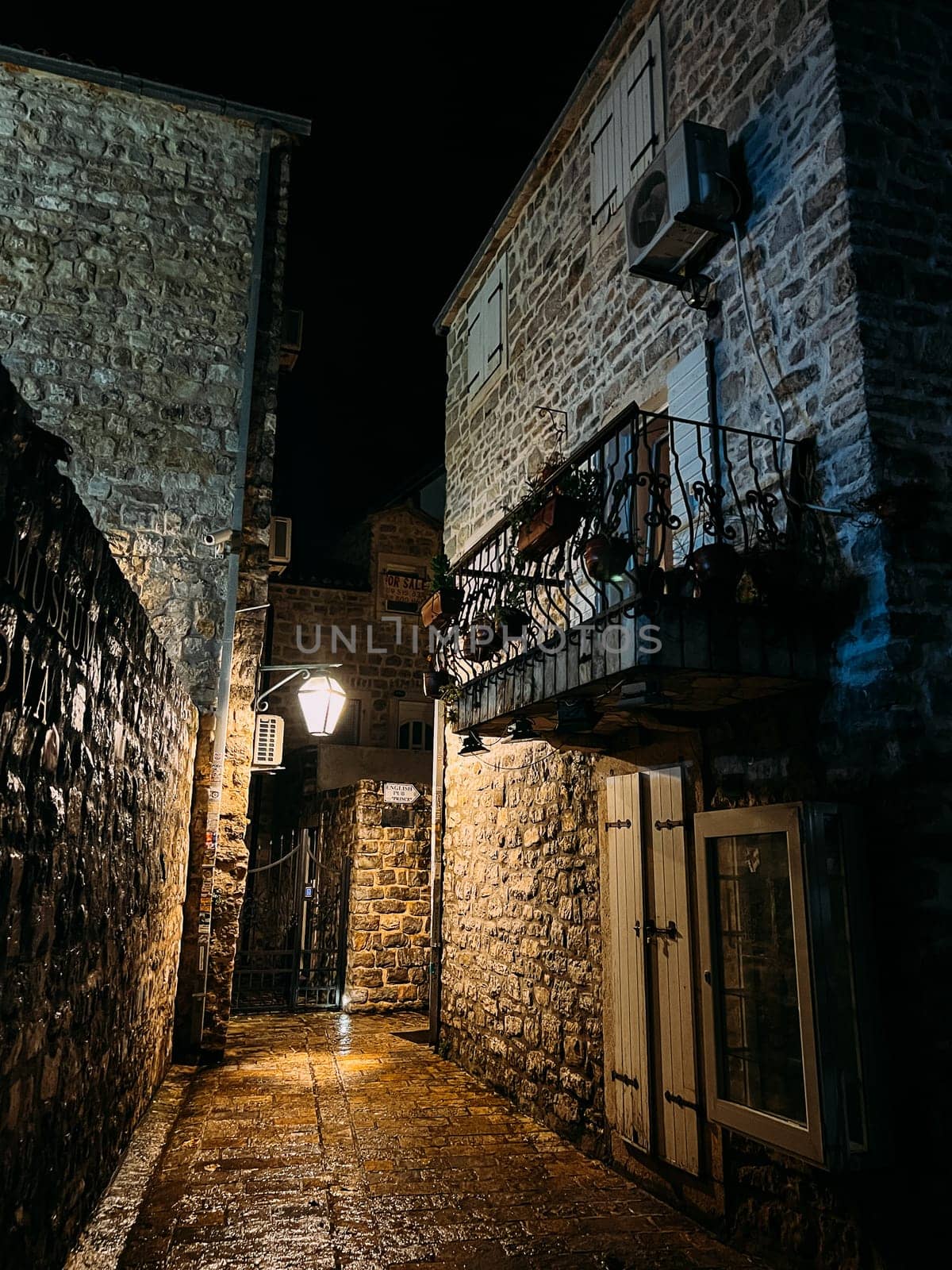 Budva, Montenegro - 25 december 2022: Narrow street between medieval houses with small balconies and shutters on the windows by Nadtochiy