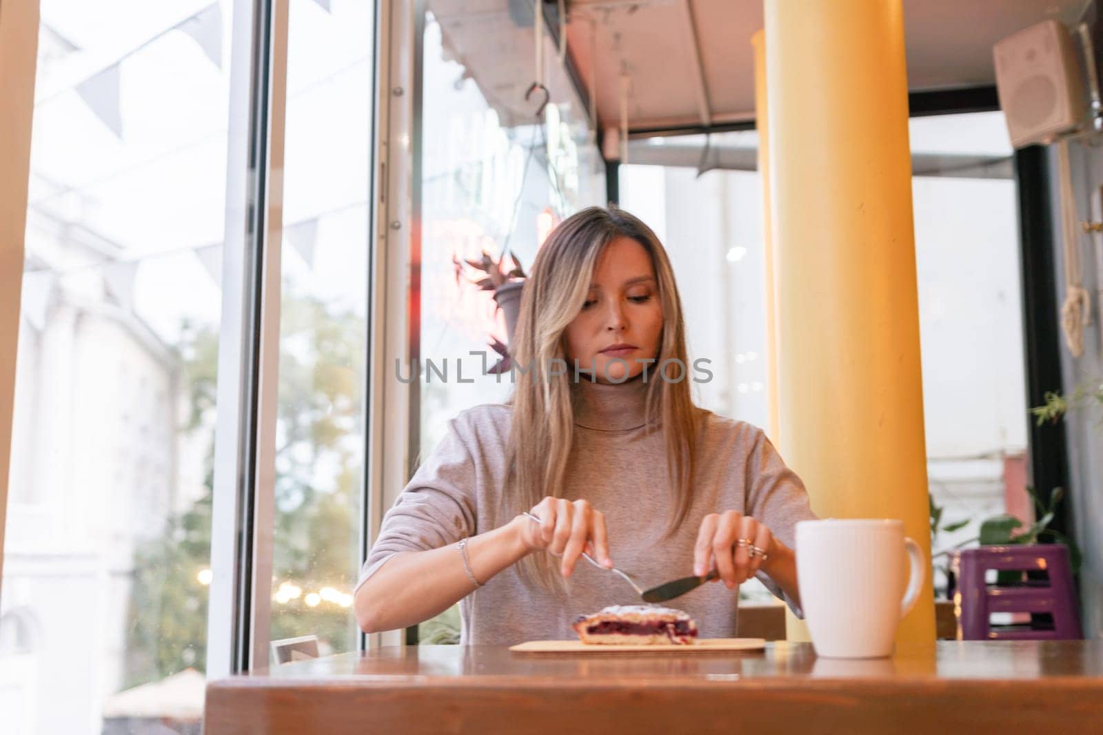 Woman with blonde hair sips cappuccino in a cafe. She is holding the glass up to her face, taking a sip of the drink