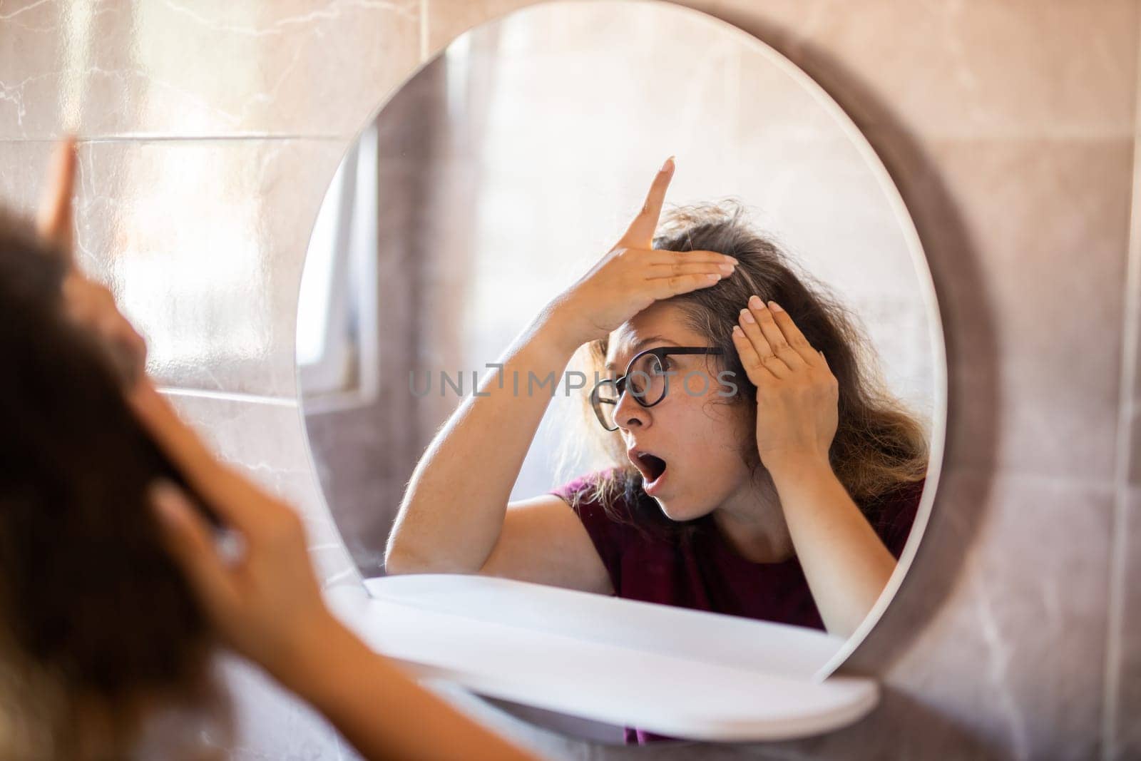 Woman Looking for Gray Hair in the Mirror. Young woman scared of premature aging signs.