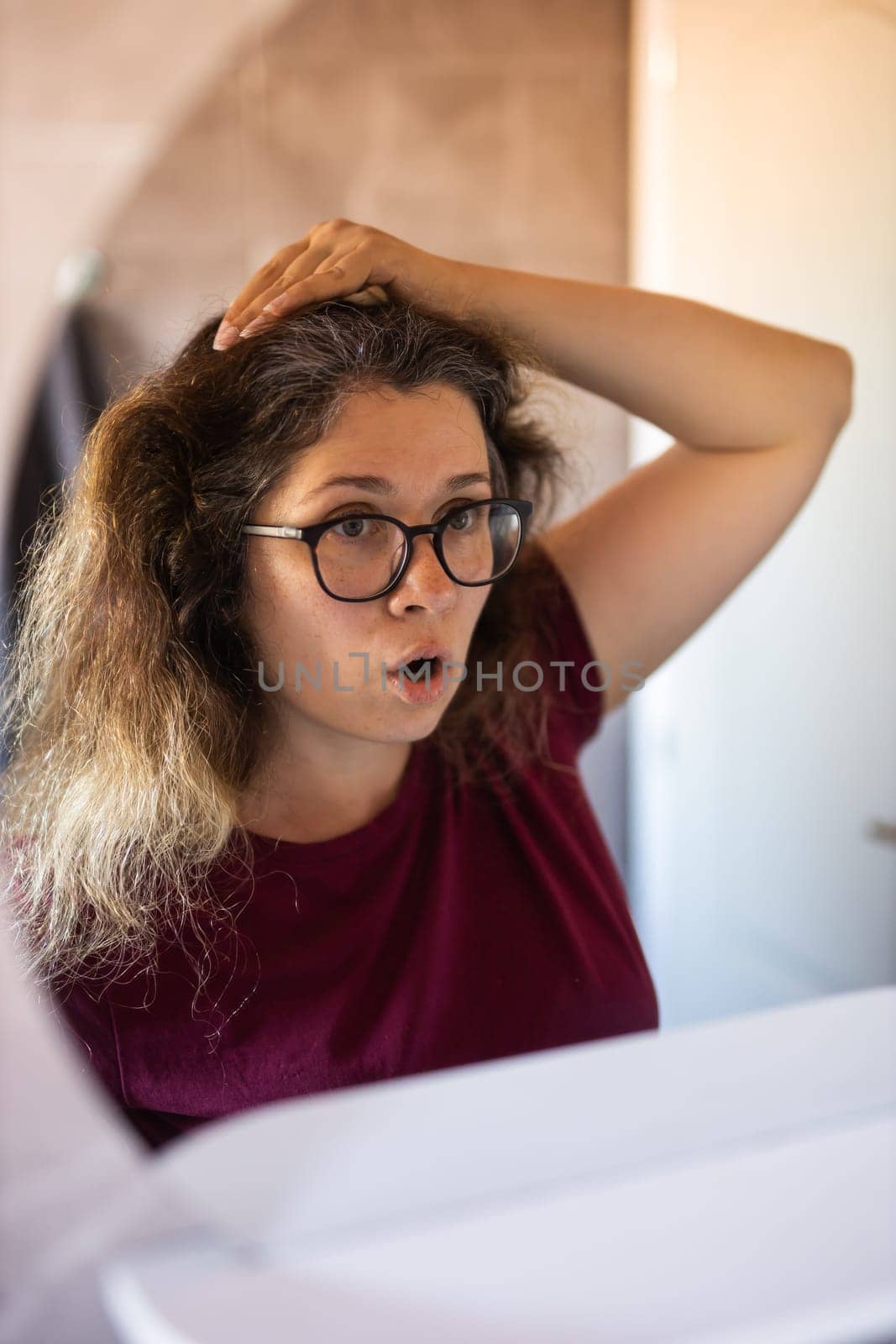 Woman Looking for Gray Hair in the Mirror. Young woman scared of premature aging signs.