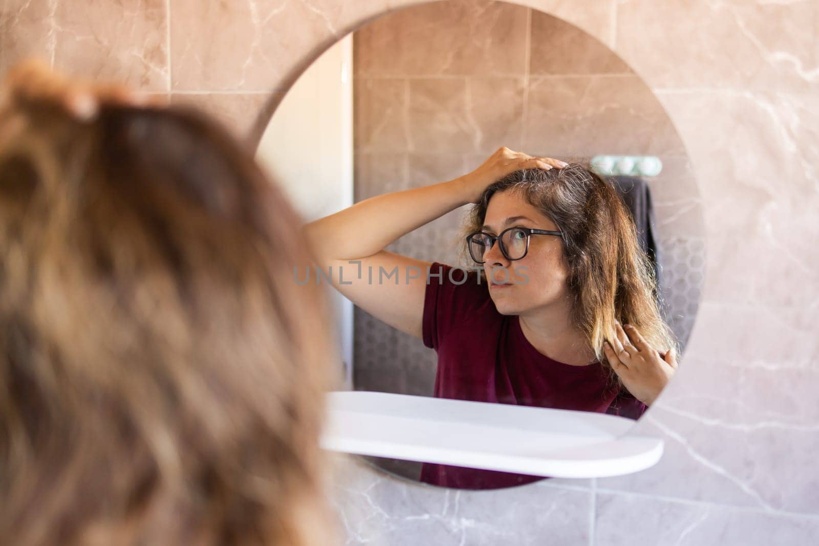 Woman Looking for Gray Hair in the Mirror. Young woman scared of premature aging signs.