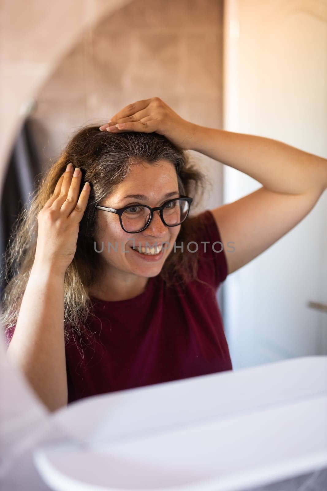 Gray haired surprised caucasian middle aged woman looking at grey hair head in mirror reflection