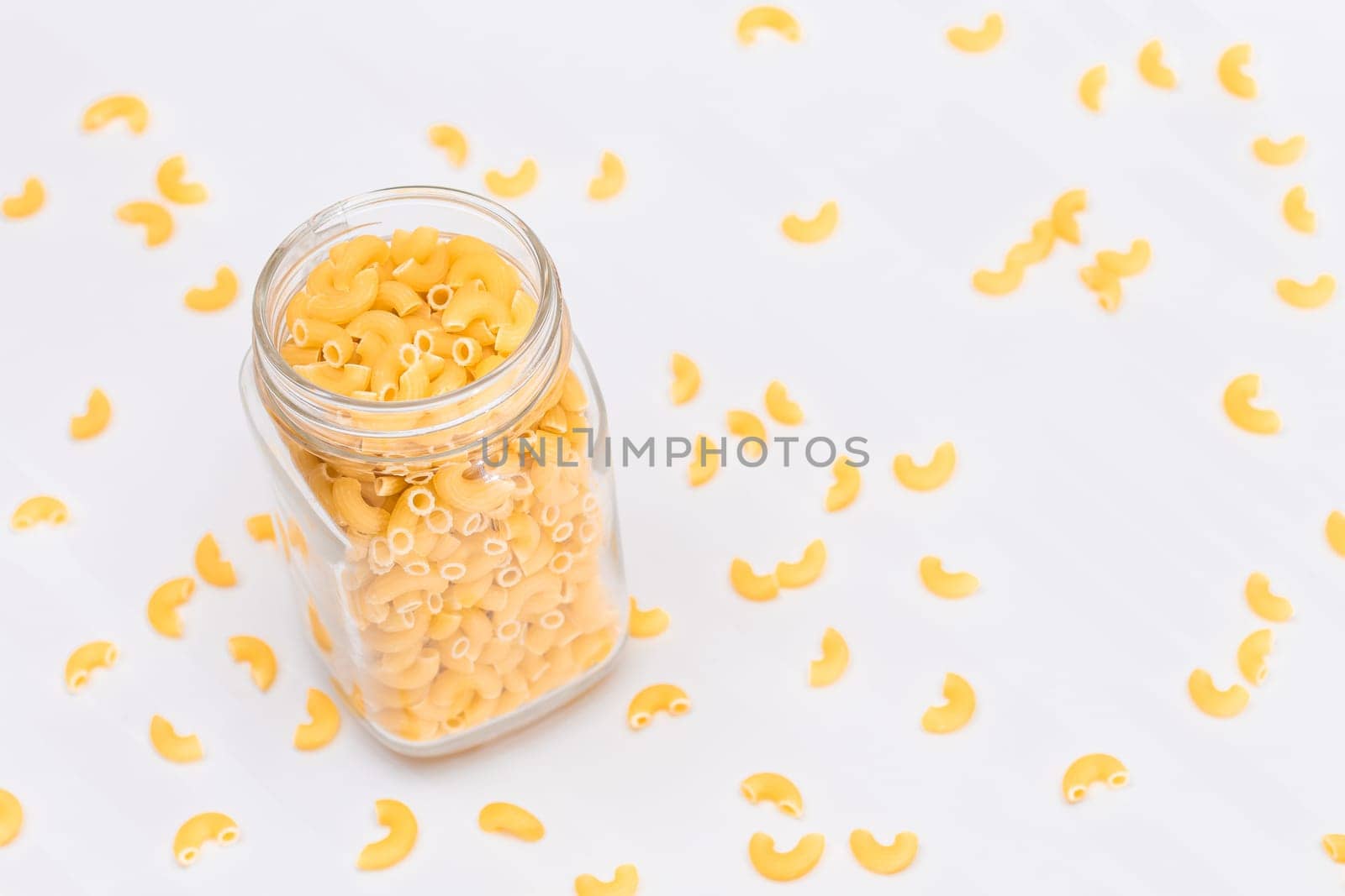 Uncooked Chifferi Rigati Pasta in Glass Jar on White Background. Fat and Unhealthy Food. Scattered Classic Dry Macaroni. Italian Culture and Cuisine. Raw Pasta