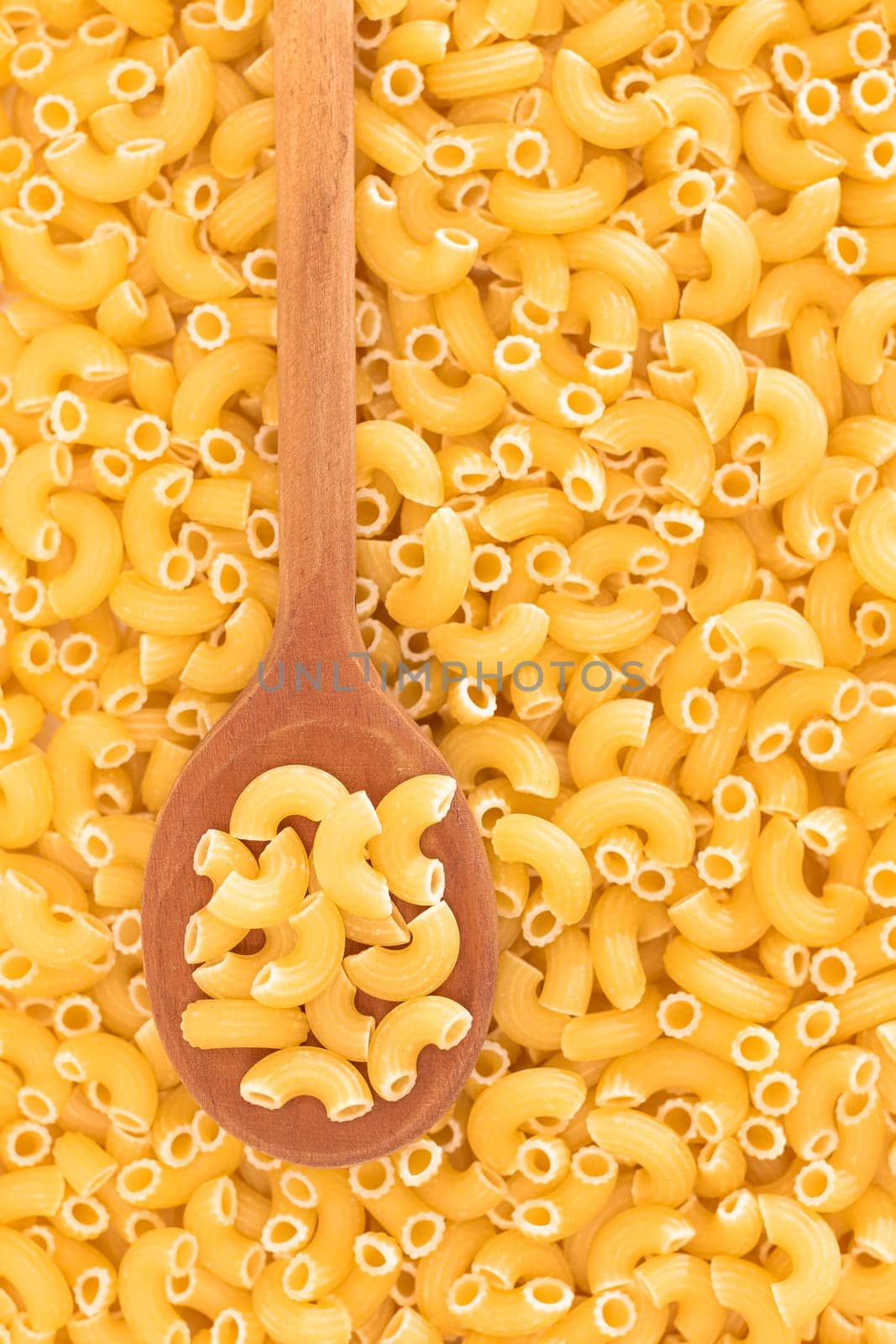 Uncooked Chifferi Rigati Pasta Background with Wooden Spoon by InfinitumProdux