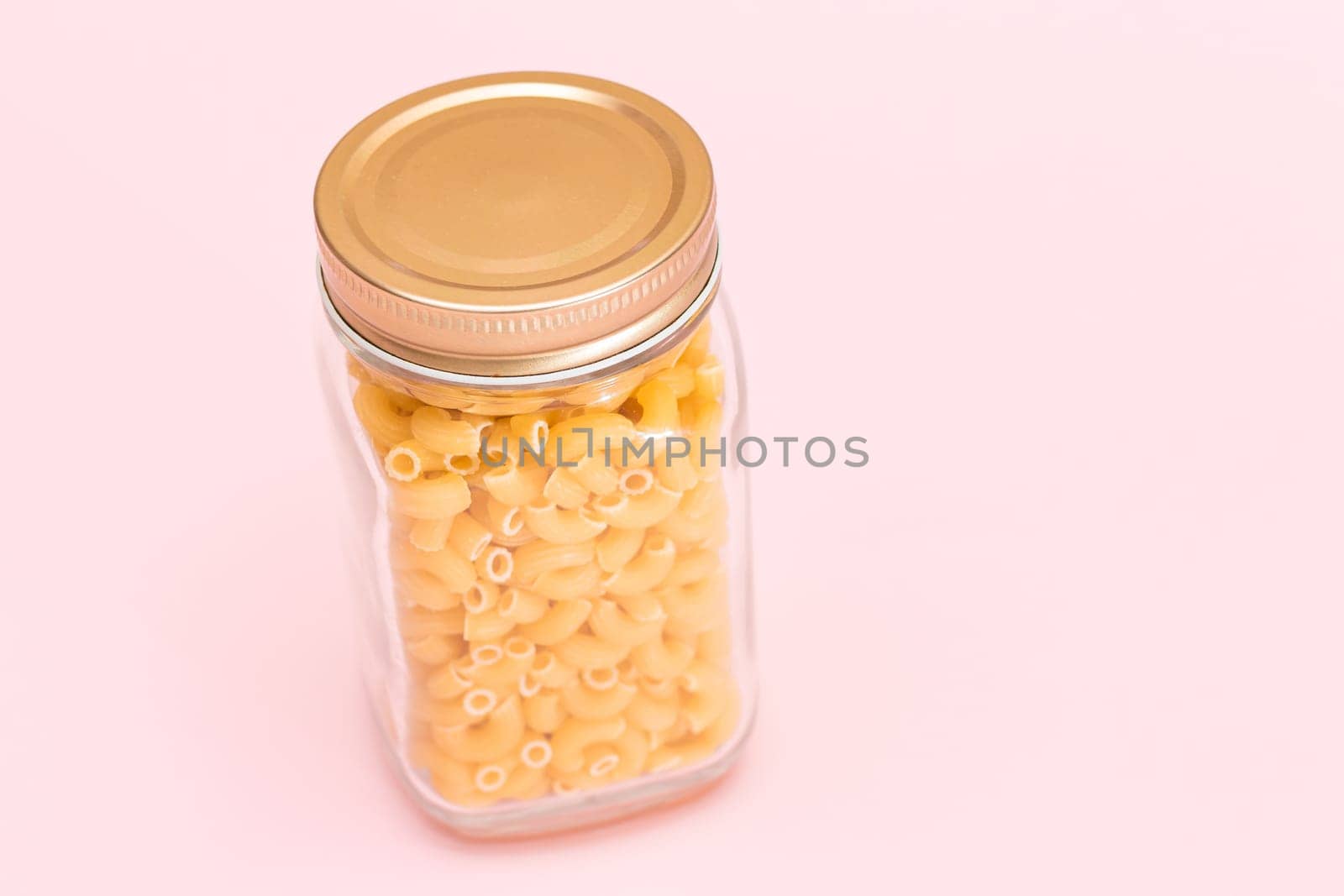 Uncooked Chifferi Rigati Pasta in Glass Jar on Pink Background by InfinitumProdux