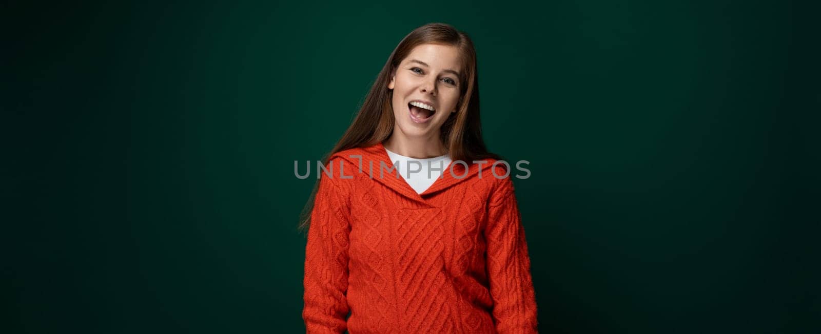 Well-groomed 30 year old woman with brown hair wears a red knitted sweater on a green background.