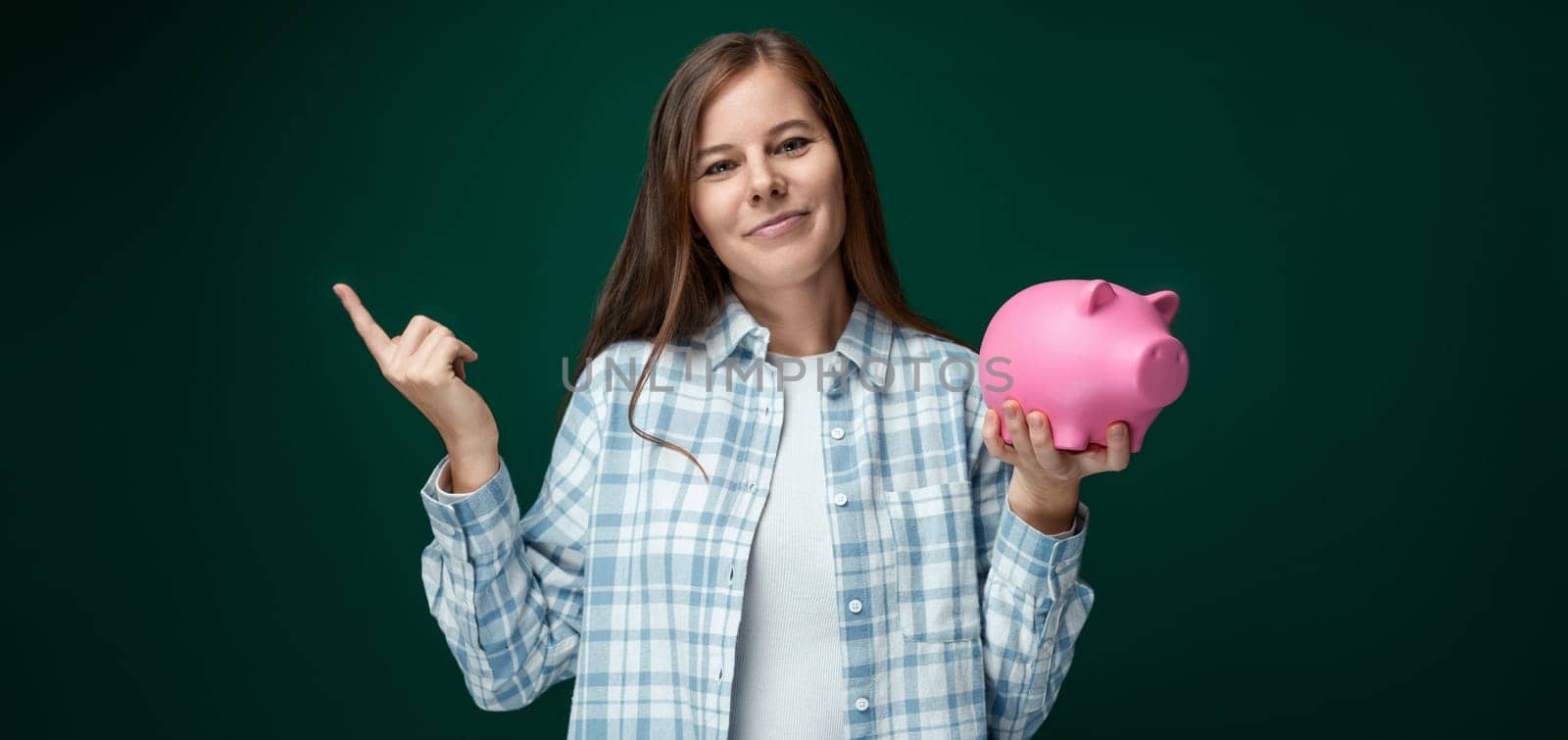 Charming young woman with brown hair holding a piggy bank and pointing her finger up.