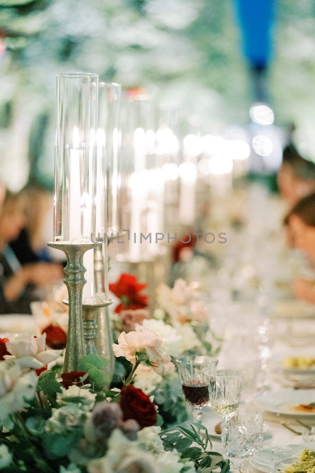 Burning candles on candlesticks with glass caps stand on a festive table among flowers. High quality photo