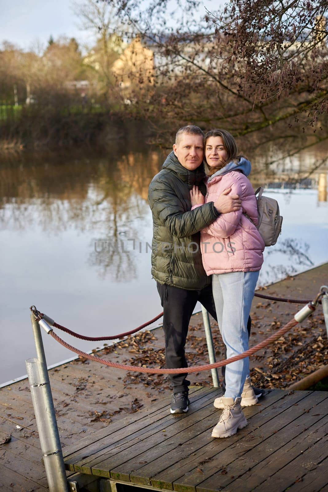 Loving couple sit on the shore of the pond in the park in autumn. A man and a woman. A couple, lovers on the shore of the lake on a walk